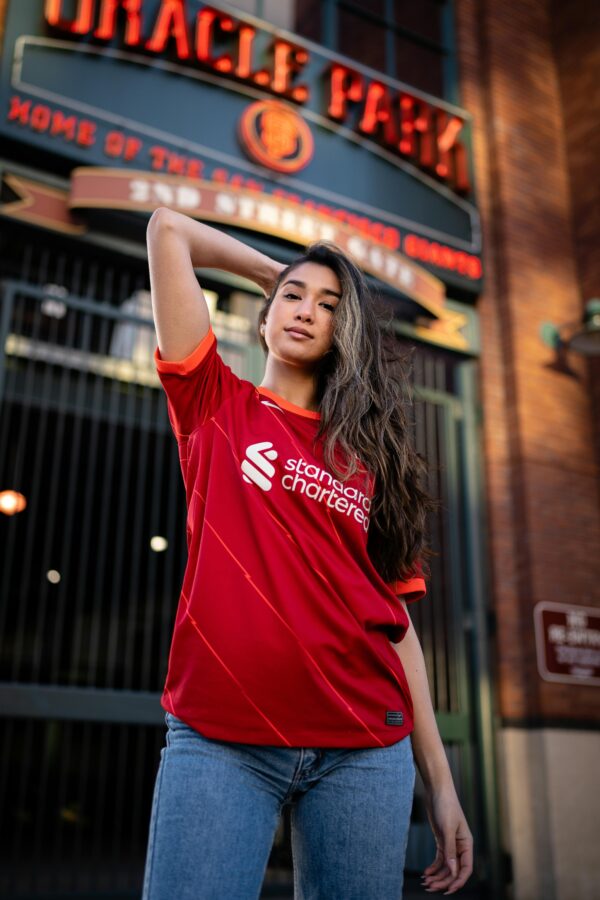 Confident woman posing in a Liverpool FC jersey outside a stadium entrance.